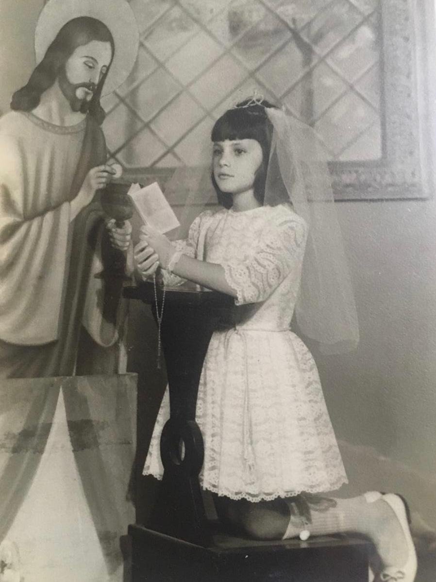 Nancy Thame criança, de véu e vestido branco, segurando um livro.